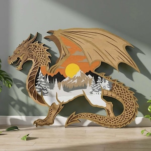 May include: A layered wooden dragon sculpture with a landscape scene inside. The dragon is brown with detailed scales and wings. The landscape features a sunset, mountains, and trees. The sculpture is displayed on a light-colored surface.
