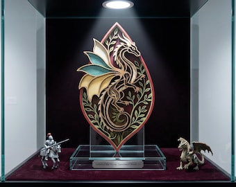 May include: A laminated wood art piece featuring a dragon design, displayed in a glass case. The dragon is intricately cut with gold, green, and blue accents. The piece is set against a dark background, with a small knight and dragon figurine.