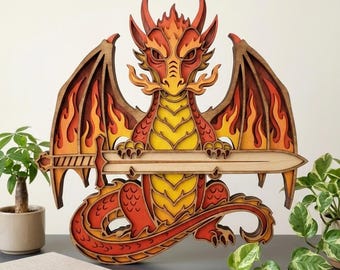 May include: A multi-layered wooden wall art piece depicting a dragon with red, orange, and yellow flame-like patterns on its wings and body. The dragon is holding a long, light-colored wooden sword horizontally across its chest with its claws.