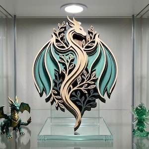 May include: A layered wooden dragon sculpture with teal and natural wood tones. The dragon has outstretched wings and is displayed on a clear glass stand. The sculpture is surrounded by other fantasy figurines.