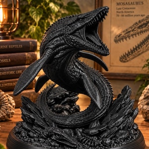 Può includere: Una statuetta nero opaco di un Mosasaurus con la bocca aperta, che rivela denti affilati e una lingua. La creatura è raffigurata in una posa di nuoto dinamica, montata su una base circolare con texture rocciose e resti fossili.