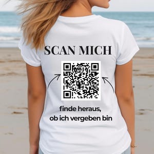 Könnte beinhalten: Weißes T-Shirt mit dem Text "SCAN MICH" und einem QR-Code auf dem Rücken. Unter dem QR-Code steht "finde heraus, ob ich vergeben bin".