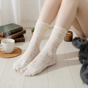 May include: Off-white lace socks with a floral design. The socks have a frilled top and are worn by a person. The socks are made of a soft, breathable material, suitable for casual wear. The socks are a fashionable accessory.