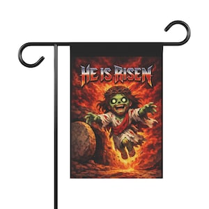 Könnte beinhalten: Eine schwarze Gartenflagge mit Metallstange und Aufhänger. Die Flagge zeigt einen Cartoon-Zombie-Jesus mit dem Text "HE IS RISEN" in einem Metall-Schriftstil. Der Hintergrund ist feurig orange und rot.