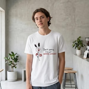 Może przedstawiać: Biały t-shirt z krótkim rękawem z ręcznie rysowaną grafiką przedstawiającą czarno-białego królika z czerwonymi akcentami. Nadrukowany czarno-czerwony napis głosi: "Don't worry, I'm just mentally unstable!". Koszulka posiada okrągły dekolt.