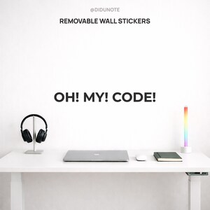 May include: A white desk with a laptop, mouse, notebook, and a multi-coloured LED light. Black headphones sit on a silver stand. The text "OH! MY! CODE!" and "REMOVABLE WALL STICKERS" are displayed.