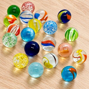 May include: A collection of nineteen spherical glass marbles in various colors and patterns. The set includes clear marbles with internal swirls of red, orange, blue, yellow, and green, as well as solid, speckled, and confetti-style glass spheres.