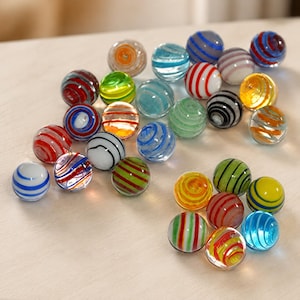 May include: A collection of spherical glass marbles featuring various colorful designs, including translucent and opaque finishes with swirling patterns, stripes, and bands in red, blue, green, yellow, orange, white, black, and grey colors.