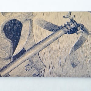 May include: A rectangular, sepia-toned artwork featuring a detailed illustration of a key inserted into a keyhole. The key and keyhole are rendered in a dark blue hue against a textured, light brown background, evoking a vintage aesthetic.