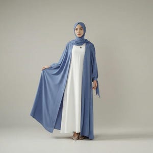 May include: A woman wearing a light blue open-front abaya over a white dress, paired with a matching headscarf. The abaya has long sleeves and a flowing design. The outfit is modest and elegant, suitable for special occasions.