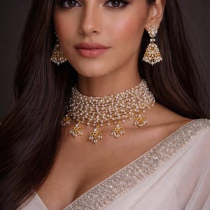 May include: A gold-toned necklace and matching earrings set. The necklace is a multi-strand design with small, round pearls and gold accents. The earrings are a similar style, with a teardrop shape. The jewelry is worn with a white garment.