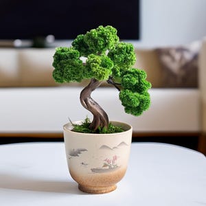 Könnte beinhalten: Ein dekorativer Bonsai-Baum mit leuchtend grünem Laub und einem geschwungenen braunen Stamm, gepflanzt in einem beigen Keramikgefäß. Der Topf zeigt eine gemalte Landschaft mit Bergen, einem kleinen Boot und rosa Blüten auf einem braunen Sockel.