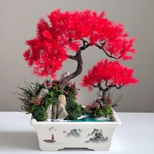 Pode incluir: Um bonsai decorativo com duas árvores de folhagem vermelha vibrante, musgo verde e rochas cinzentas num vaso de cerâmica retangular branco. O vaso está decorado com uma paisagem pintada que mostra um barco e montanhas.
