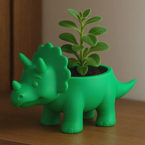 May include: A bright green triceratops dinosaur planter featuring a smooth matte finish. The dinosaur has a large frill, three horns, and a short tail. A small green succulent plant with oval leaves is planted in the opening on its back.