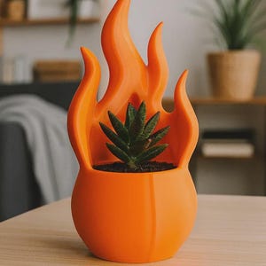 May include: A bright orange planter shaped like a stylized flame, featuring a smooth, rounded base and pointed, upward-reaching flame-like extensions. A small, dark green succulent plant with pointed leaves is potted inside the center of the container.