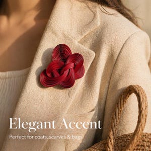 Pode incluir: Um broche vermelho tecido com um design floral é preso a um blazer bege. O texto "Elegant Accent" é exibido abaixo. O broche é um acessório decorativo para casacos, lenços e bolsas.