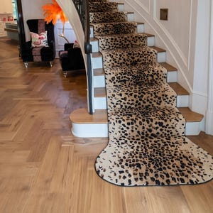 Könnte beinhalten: Eine geschwungene Treppe mit einem Teppichläufer mit Leopardenmuster. Die Stufen haben weiße Setzstufen und Holzstufen. Ein schwarzes schmiedeeisernes Geländer verläuft entlang der Wand. Die Wände sind weiß mit dekorativen Paneelen.