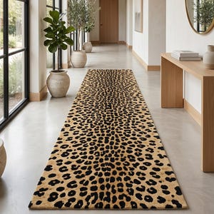 Peut inclure: Un long tapis de couloir rectangulaire présentant un motif léopard répétitif avec des taches noires sur un fond beige. Le tapis est placé au centre sur un sol lisse de couleur claire, s'étendant du premier plan vers le fond de l'espace.