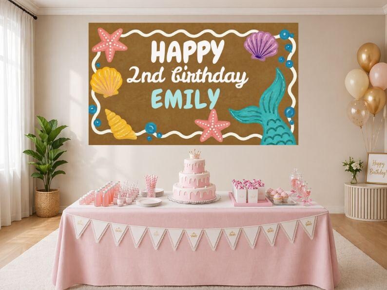 May include: A birthday party scene with a pink tablecloth, a banner, and a three-tiered cake. A large brown banner displays the text "HAPPY 2nd birthday EMILY" with mermaid and seashell illustrations. Balloons and party supplies are also visible.