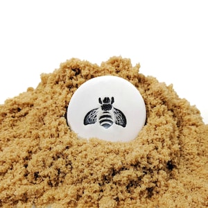 May include: A white ceramic bee-shaped bottle stopper sits on a pile of brown sugar.