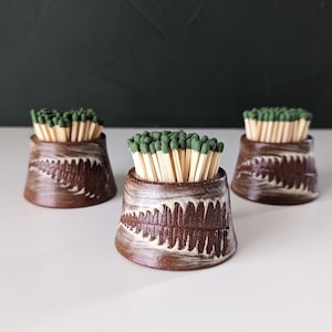 May include: Three ceramic matchstick holders with a fern pattern. Each holder is filled with green-tipped matches.