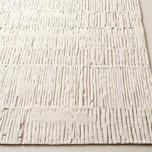 Puede incluir: Alfombra rectangular de color crema con una superficie texturizada. La alfombra presenta un patr&oacute;n de l&iacute;neas verticales, creando un efecto rayado. Las l&iacute;neas est&aacute;n ligeramente elevadas, agregando profundidad e inter&eacute;s visual al dise&ntilde;o de la alfombra. La alfombra est&aacute; hecha de un material suave y afelpado.