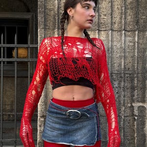 Peut inclure: Un haut rouge &agrave; manches longues en maille ajour&eacute;e avec un design d&eacute;chir&eacute;. Il est associ&eacute; &agrave; un crop top noir, une mini-jupe en jean avec une boucle argent&eacute;e et des collants rouges. Une tenue audacieuse.