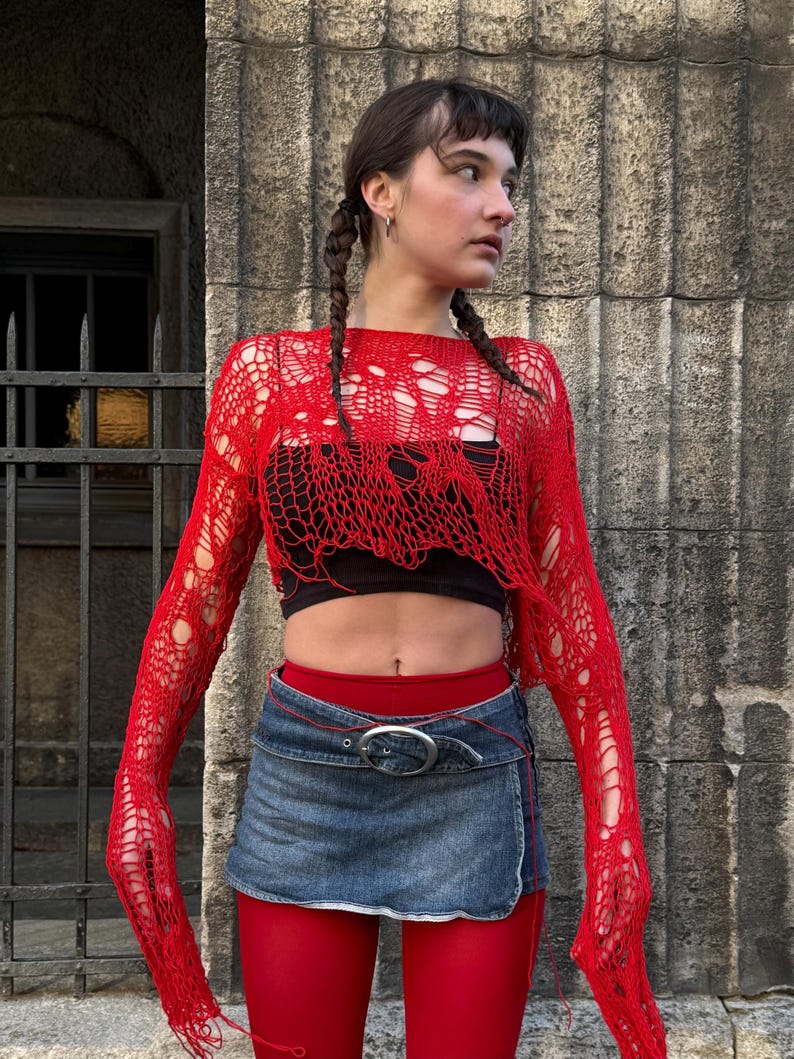 Peut inclure: Un haut rouge &agrave; manches longues en maille ajour&eacute;e avec un design d&eacute;chir&eacute;. Il est associ&eacute; &agrave; un crop top noir, une mini-jupe en jean avec une boucle argent&eacute;e et des collants rouges. Une tenue audacieuse.