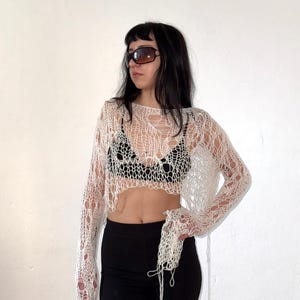 Peut inclure: Haut en tricot ajour&eacute; blanc cass&eacute; &agrave; manches longues. Le haut a un design ample et a&eacute;r&eacute;. Le mod&egrave;le porte un legging noir et des lunettes de soleil. Le haut est un v&ecirc;tement unique, fait &agrave; la main.