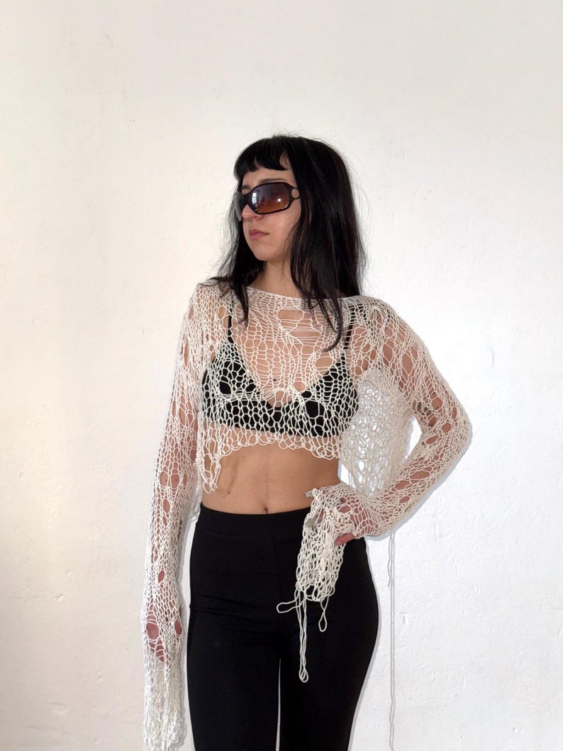 Peut inclure: Haut en tricot ajour&eacute; blanc cass&eacute; &agrave; manches longues. Le haut a un design ample et a&eacute;r&eacute;. Le mod&egrave;le porte un legging noir et des lunettes de soleil. Le haut est un v&ecirc;tement unique, fait &agrave; la main.
