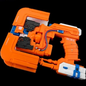 May include: An orange and white toy gun with the text "RX-78-Z" printed on the side. The toy gun has a blue wire and accents, and black details. The toy gun is set against a black background.