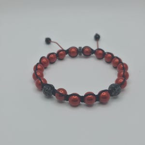 Peut inclure: Bracelet de perles rouges avec cordon noir et deux perles d'accent noires et argent&eacute;es. Le bracelet est r&eacute;glable et repose sur un fond blanc. Un accessoire &eacute;l&eacute;gant.
