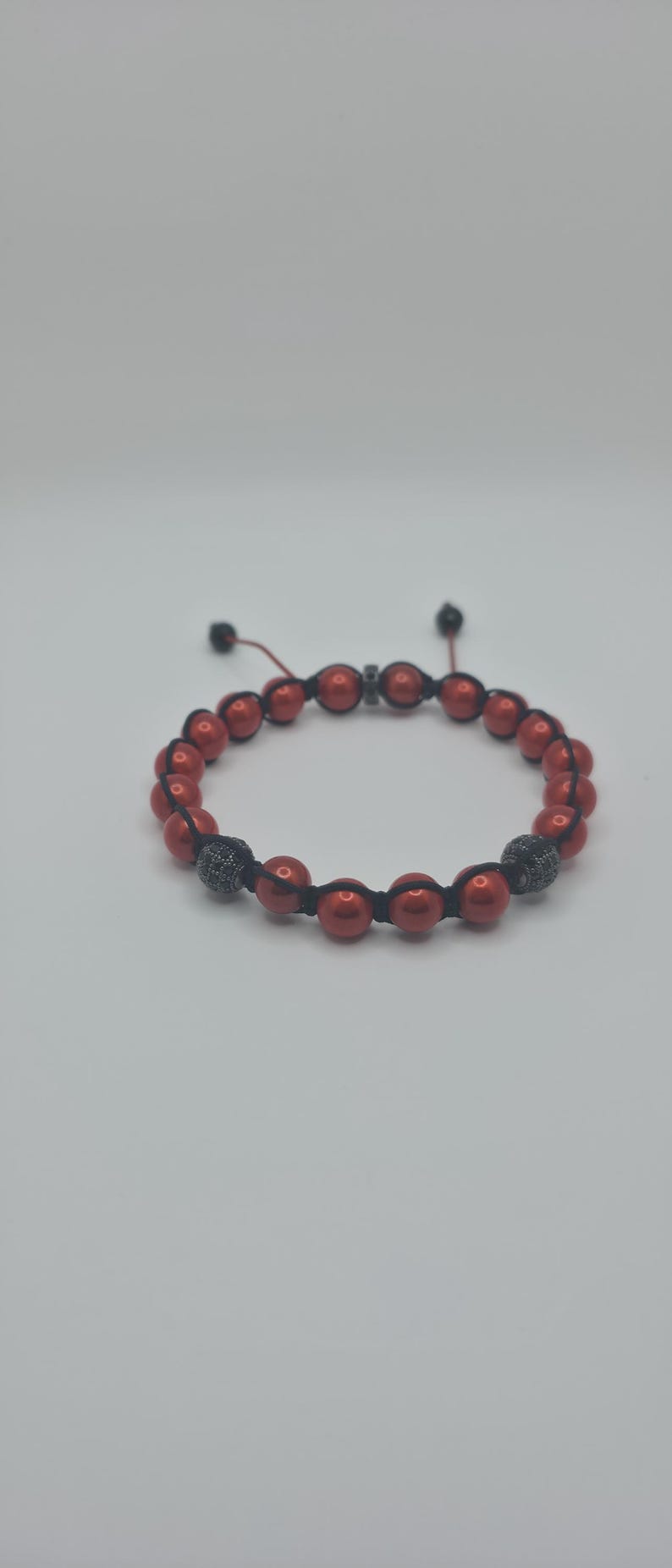 Peut inclure: Bracelet de perles rouges avec cordon noir et deux perles d'accent noires et argent&eacute;es. Le bracelet est r&eacute;glable et repose sur un fond blanc. Un accessoire &eacute;l&eacute;gant.