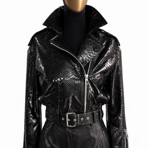 Könnte beinhalten: Ein Set aus drei Keramikbechern mit gesprenkelter, cremefarbener Glasur. Jeder Becher zeigt ein handgemaltes Design: ein blau-grünes Blatt, eine gelbe Blume und eine rote Beere. Die Becher haben eine einfache, abgerundete Form.