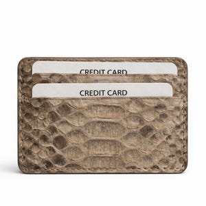 May include: A rectangular cardholder with a snakeskin-like texture in brown and tan hues. Two white cards, marked "CREDIT CARD", are visible. The cardholder features rounded corners and a stitched edge.