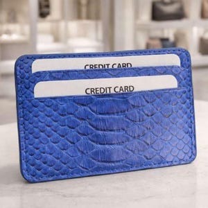 Op de afbeelding: Blauwe kaarthouder met een slangenleertextuur. Twee witte creditcards zijn zichtbaar, elk met de tekst "CREDIT CARD". De kaarthouder is rechthoekig met afgeronde hoeken.