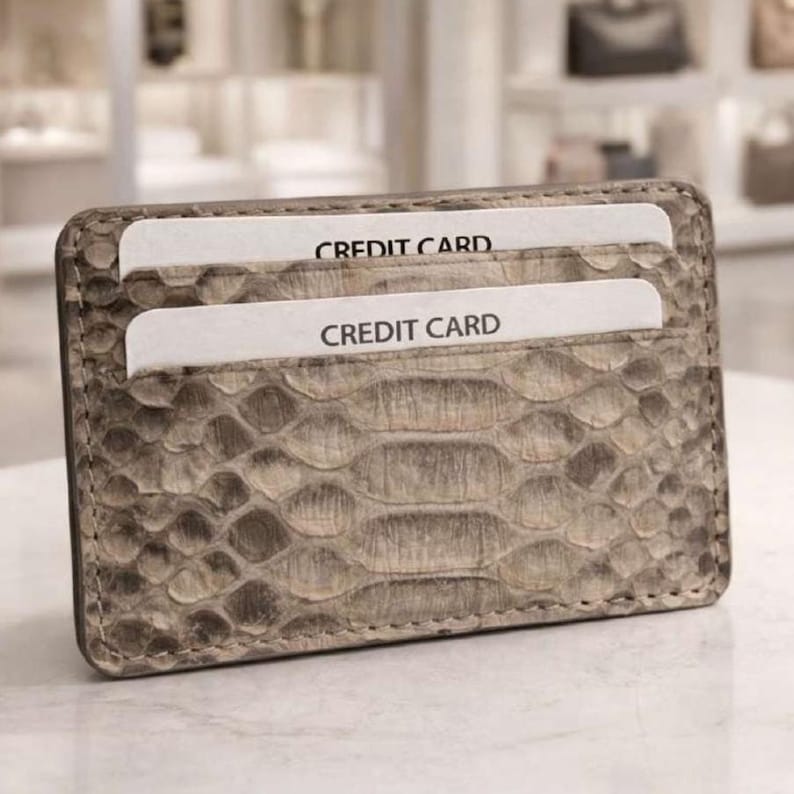 Op de afbeelding: Een rechthoekige kaarthouder met een textuur die op slangenleer lijkt, in grijstinten en beige. Twee witte kaarten met de tekst "CREDIT CARD" zijn zichtbaar. De kaarthouder is ontworpen om creditcards in te bewaren.