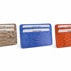 Op de afbeelding: Drie leren kaarthouders in bruin, blauw en oranje, elk met een reptielenhuidtextuur. Elke portemonnee heeft twee sleuven met "CREDIT CARD" gedrukt op de kaarten erin. De portemonnees worden tegen een witte achtergrond weergegeven.
