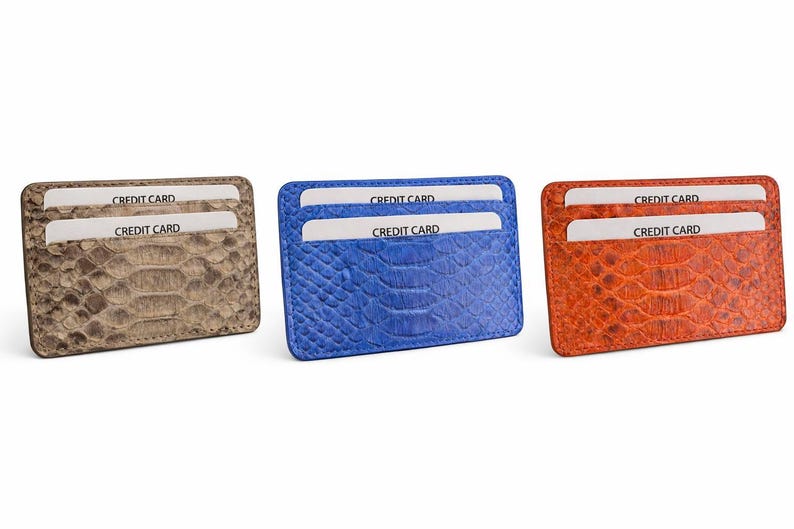 Op de afbeelding: Drie leren kaarthouders in bruin, blauw en oranje, elk met een reptielenhuidtextuur. Elke portemonnee heeft twee sleuven met "CREDIT CARD" gedrukt op de kaarten erin. De portemonnees worden tegen een witte achtergrond weergegeven.