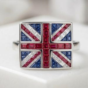 May include: A square-faced ring featuring a Union Jack design. The ring's face is meticulously crafted with red, white, and blue gemstones, arranged to replicate the British flag. The ring has a silver band.