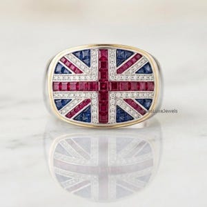 Puede incluir: Un anillo con una cara rectangular diseñada como la bandera de la Union Jack. El diseño se compone de rubíes rojos y zafiros azules de corte cuadrado engastados en canal, acentuados por filas de pequeños diamantes blancos en una banda metálica.