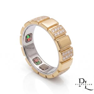 May include: A gold-toned smart ring featuring a segmented outer band with alternating smooth panels and sections encrusted with small clear stones. The inner surface is silver-toned with visible electronic sensors and the text PierceLab.
