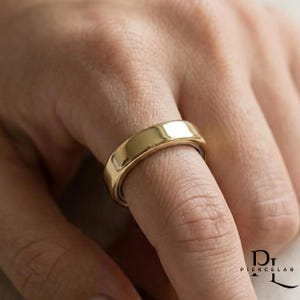 May include: A polished gold band ring with a smooth, reflective surface and a rounded profile. The ring features a simple, solid design with no additional embellishments, stones, or engravings, showcasing a clean and uniform metallic finish.