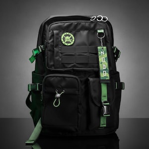 May include: A black backpack featuring green accents, a circular patch with a skull and swords, and a hanging fabric tag with the text ZORO. The bag includes multiple zippered compartments, side release buckles, mesh pockets, and adjustable straps.