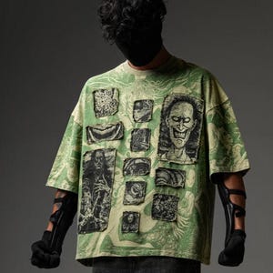 May include: A light green short-sleeve t-shirt featuring an all-over graphic print of intricate line art. The shirt is adorned with multiple rectangular fabric patches, each displaying distinct black and white illustrations of various grotesque figures.