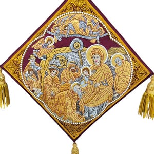 Könnte beinhalten: Gestickte religiöse Ikone mit einer zentralen Szene von Figuren in goldenen Gewändern und Heiligenscheinen, vor einem tief burgunderroten Hintergrund. Das quadratische Design ist mit goldenen Verzierungen und Quasten versehen und zeigt detaillierte Handarbeit und religiöse Bilder.
