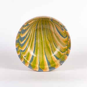 May include: A ceramic bowl with a striped pattern in shades of green, yellow, and blue. The bowl has a rounded shape and a slightly flared rim. The stripes radiate from the centre of the bowl.