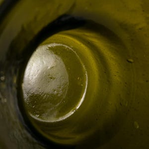 May include: Close-up of the inside of a green glass bottle. The interior is a swirling, textured surface with a dark, circular opening. The glass has a slight yellowish tint.
