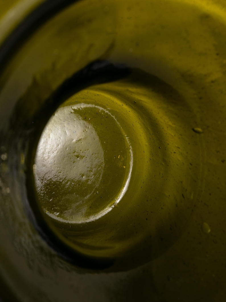May include: Close-up of the inside of a green glass bottle. The interior is a swirling, textured surface with a dark, circular opening. The glass has a slight yellowish tint.