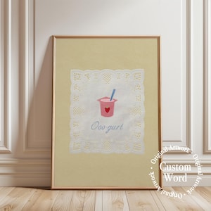 Può includere: Una stampa artistica incorniciata su sfondo beige chiaro che presenta un centrino di pizzo bianco centrato con l'illustrazione di un vasetto di yogurt rosa, una piccola icona di fragola rossa, un cucchiaio blu e il testo blu Ooo-gurt.